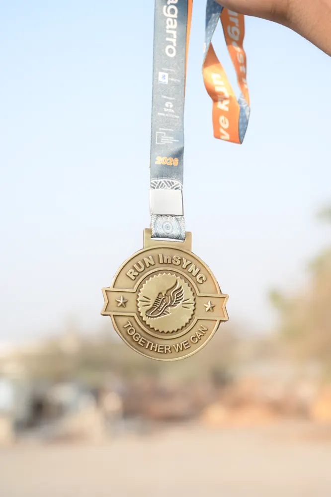 The Run InSync finisher medal held up against the morning sky